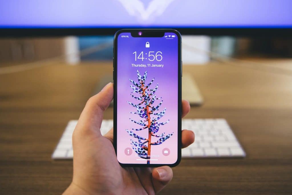 Close-up of a hand holding a smartphone with a vibrant purple screen displaying the time and date.