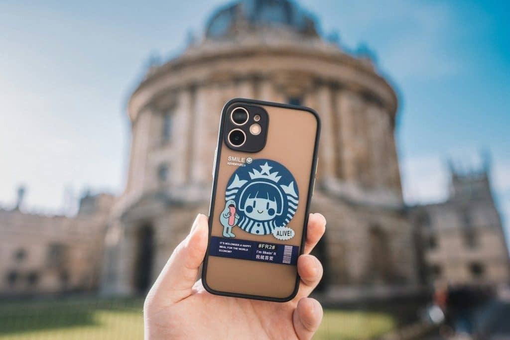 Telefon u ruci sa dekorativnom maskicom ispred gradske znamenitosti – prikaz kako maskica za telefon pruža zaštitu i personalizovan izgled uređaja.