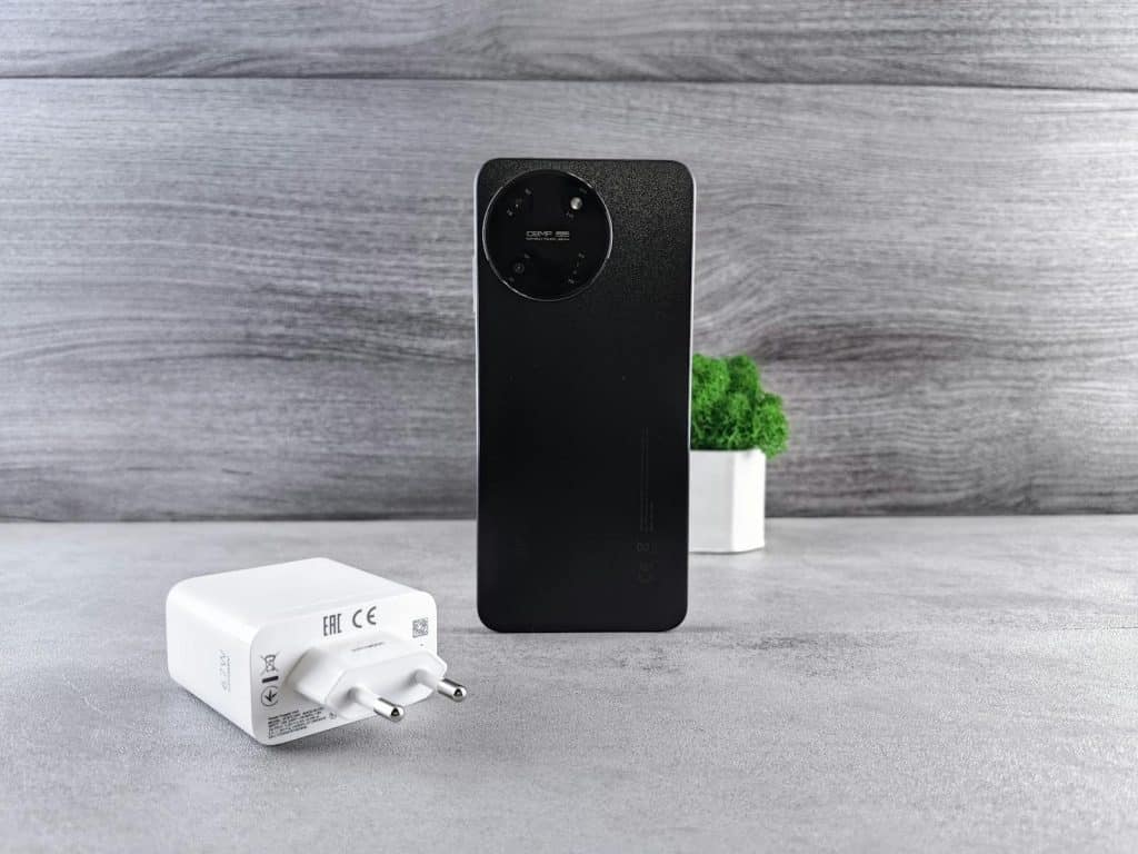 Sleek black smartphone with a charger on a textured gray surface, featuring minimalist style.