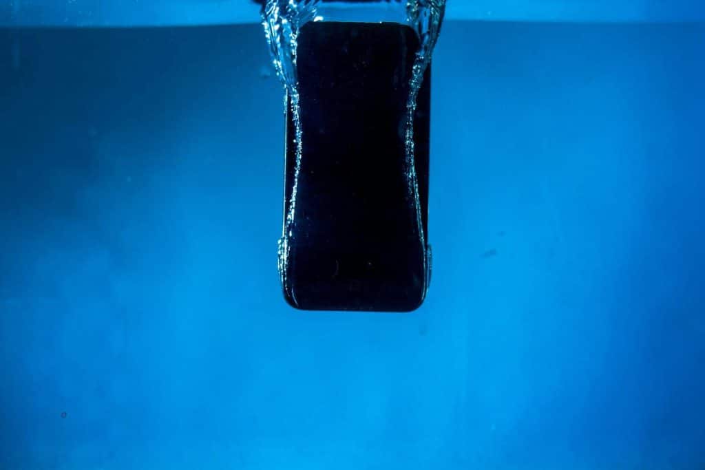 A smartphone partially submerged in water, captured against a blue backdrop.